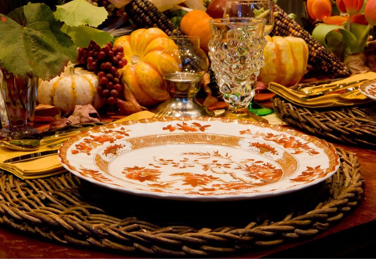 Mesa posta elegante com louça floral em tons terrosos, copo de vidro artístico e elementos naturais, representando a curadoria personalizada da Hello Mary´Experience.